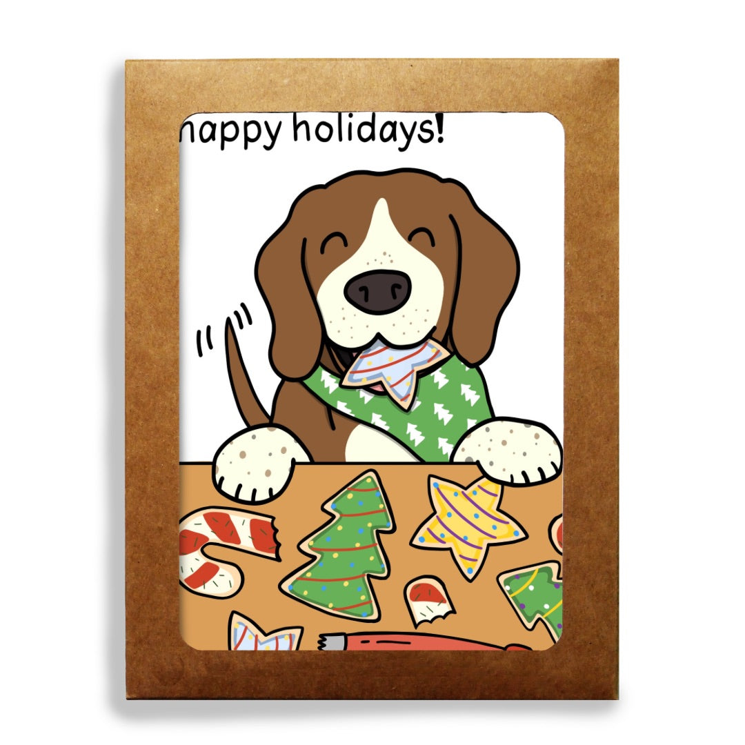 A square kraft paper holiday greeting card set featuring a cartoon beagle dog in a green bandanna behind a table with Christmas cookies, with the text 'happy holidays!' at the top, shown on a white background.