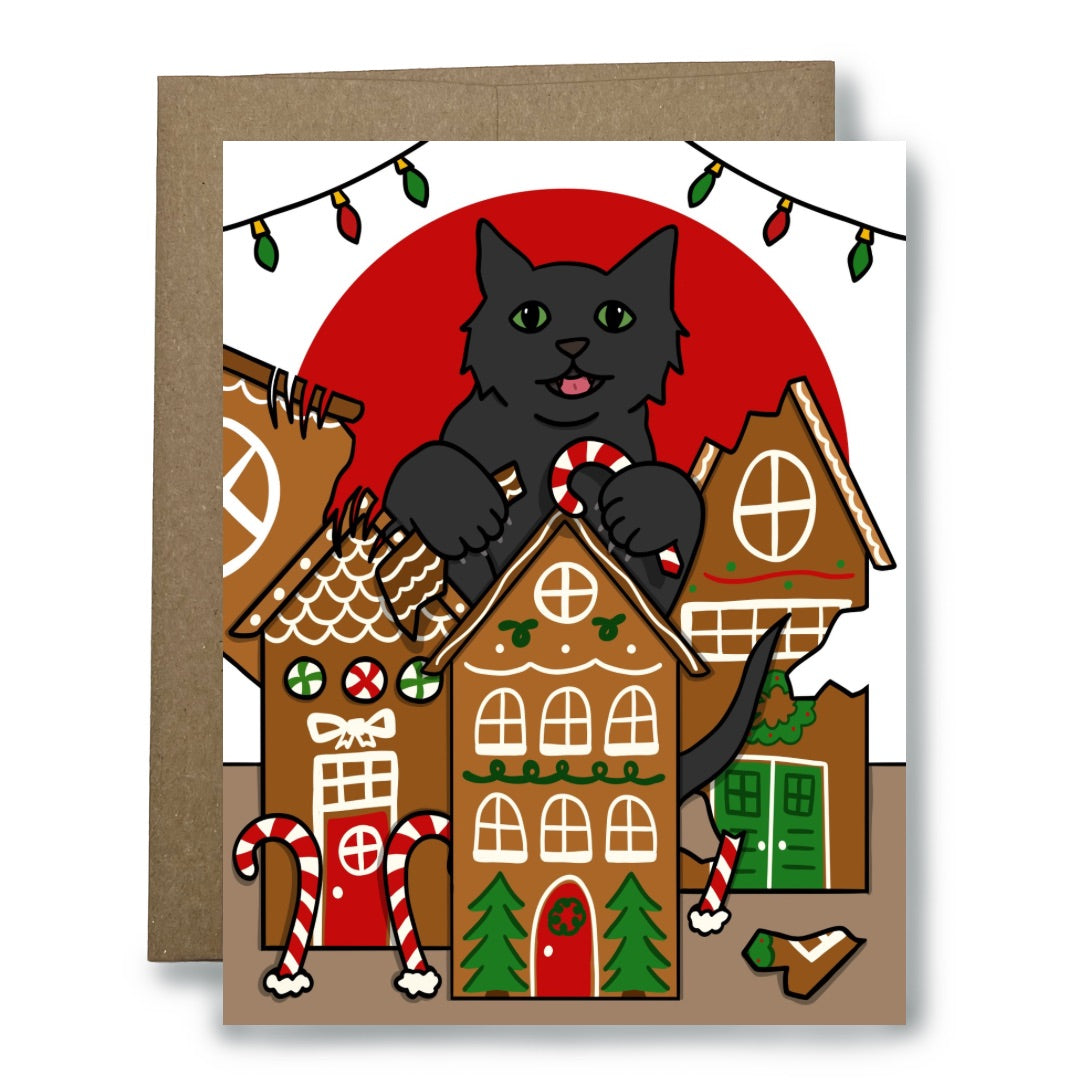 A Christmas-themed greeting card featuring a black cat destroying  gingerbread houses, with a kraft paper envelope behind it on a white background.