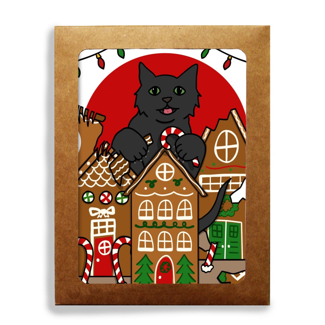 A stationery set featuring a whimsical holiday illustration of a black cat with green eyes destroying gingerbread houses, holding candy canes, with a large red sun and Christmas lights in the background.