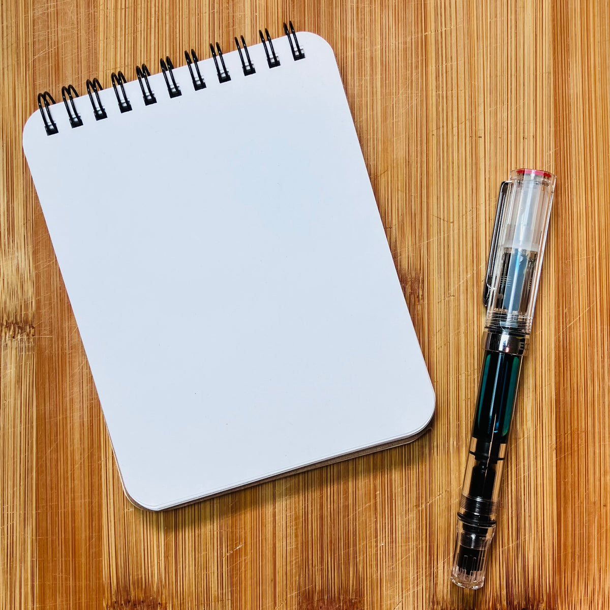 Open notebook showing blank interior page and a pen, photographed against warm wood background