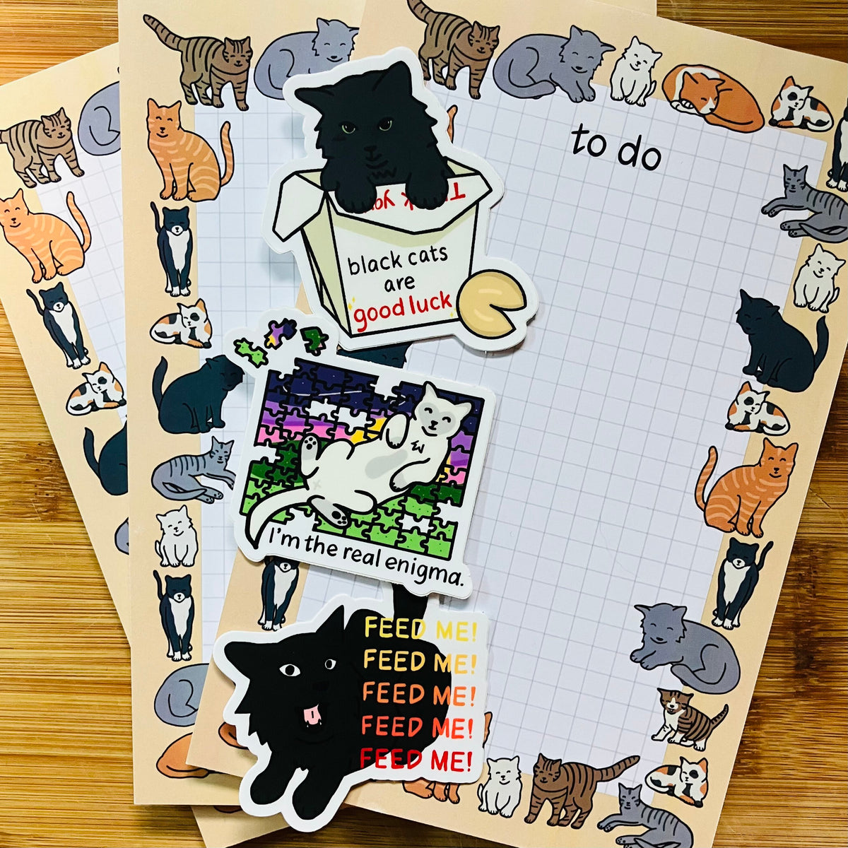 Three cat-themed to do lists with a center grid pattern and border of colorful illustrations of various cat breeds next to three cat stickers.