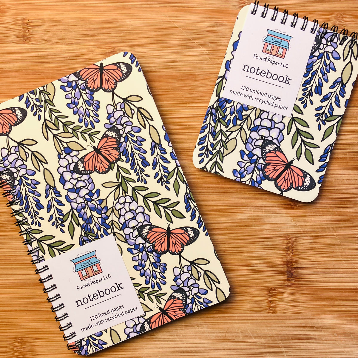 Two notebooks with butterfly and wisteria design, photographed against warm wood background