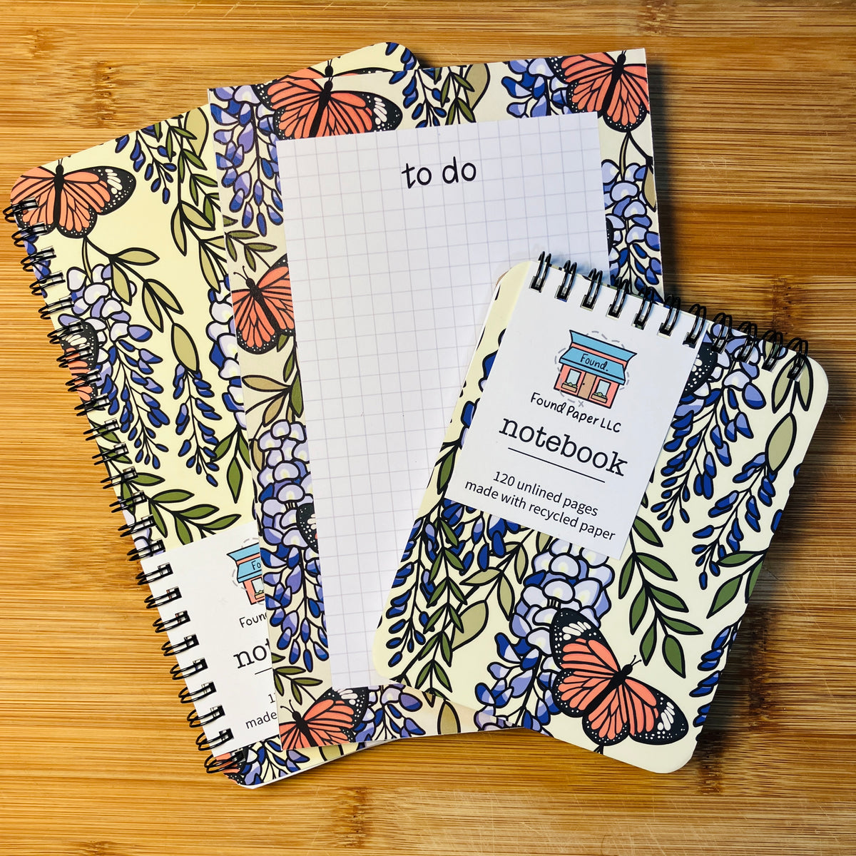 Two notebooks and a to do pad with butterfly and wisteria design, photographed against warm wood background